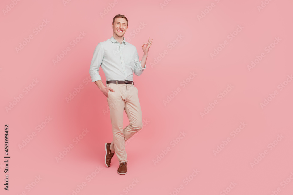 Full length photo of young man happy positive smile show okay alright deal done sign isolated on pink color background Full length photo of young man happy positive smile show okay alright deal done sign isolated on pink color background