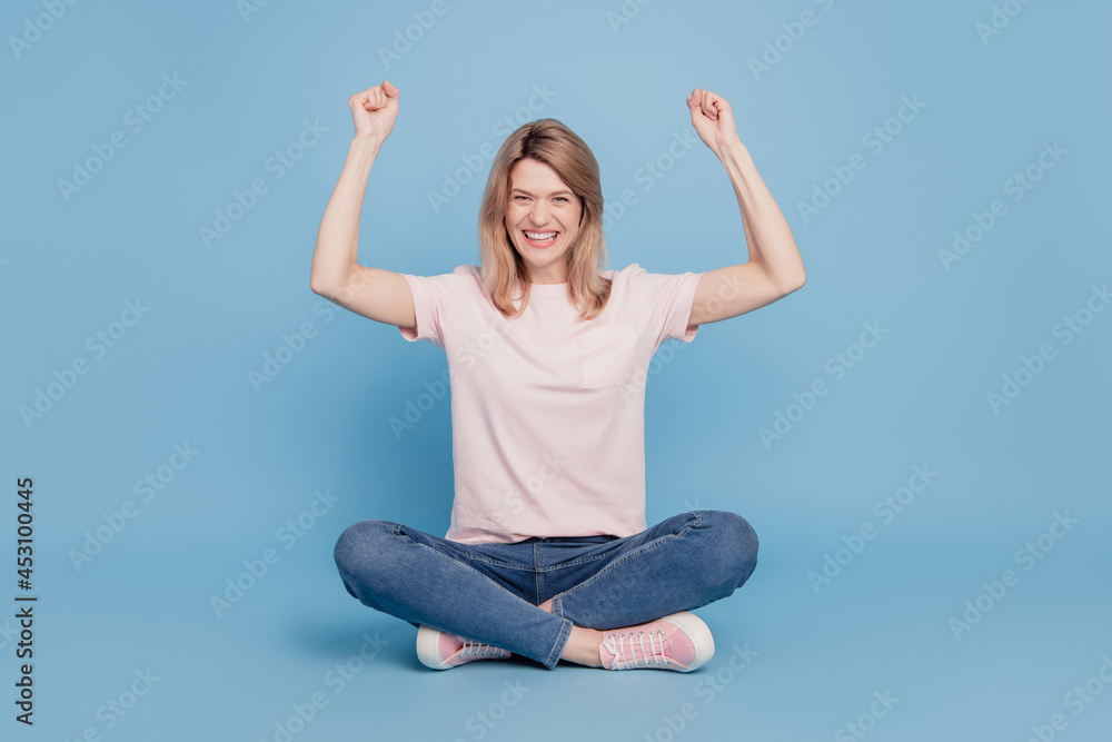 Portrait of astonished excited girl sit floor raise fists celebrate victory on blue background Portrait of astonished excited girl sit floor raise fists celebrate victory on blue background