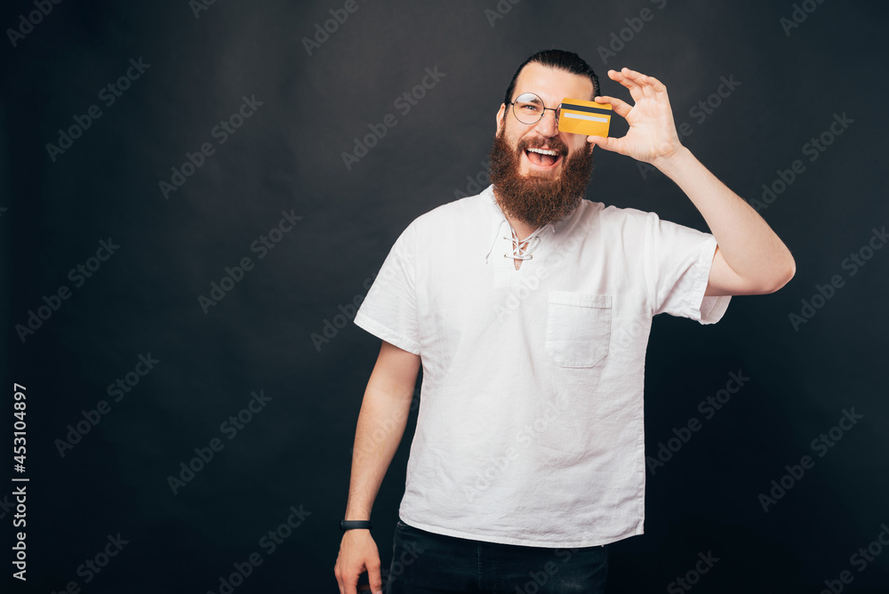 Naklejka premium Excited bearded man is covering one eye with a credit card.