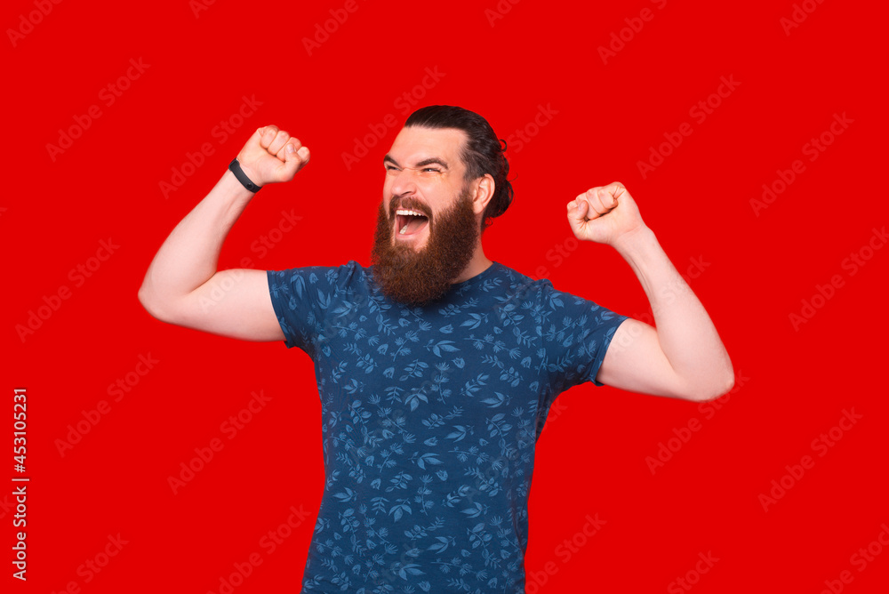 Screaming bearded man is making the winner gesture over red background. Screaming bearded man is making the winner gesture over red background.