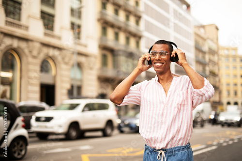 Cheerful guy listening the music with the headphones. Young african man walking through the city