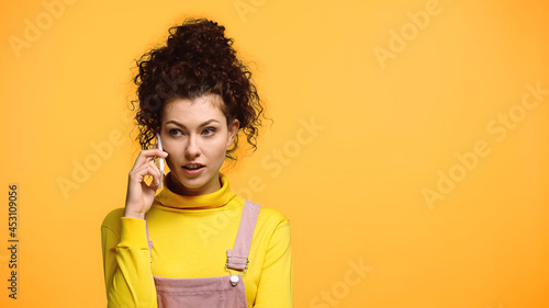 concentrated woman talking on mobile phone isolated on orange