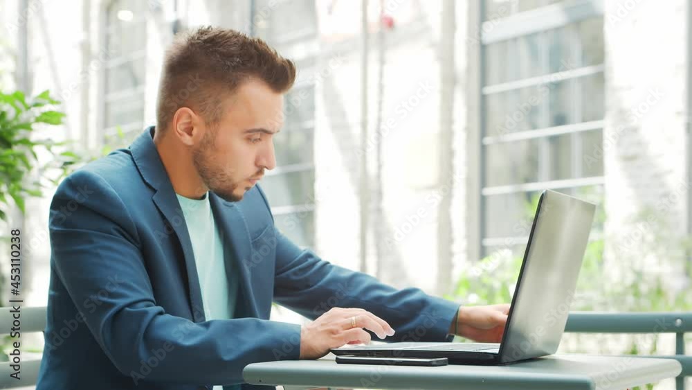 Young successful caucasian businessman works in an outdoor cafe using a computer. Business, freelance and remote work. Young successful caucasian businessman works in an outdoor cafe using a computer. Business, freelance and remote work.