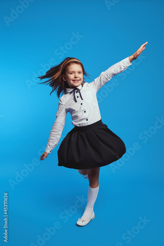 Full body photo of playful schoolgirl spinning fast in school uniform dress, causing it to flare out. Studio shot on blue background 
