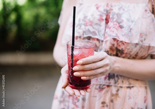 Very nice young woman holding a glass of fresh red lemonade with strawberry and basil, cropped photo close up view