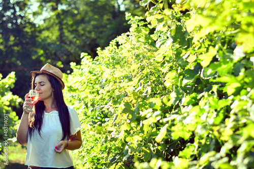 Young beautiful smiling woman walking at Vineyard with a glass of rose wine.Wine tourism