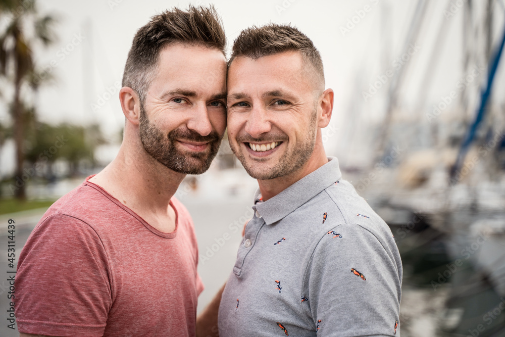 Cheerful gays embracing while looking at camera on urban road Cheerful gays embracing while looking at camera on urban road