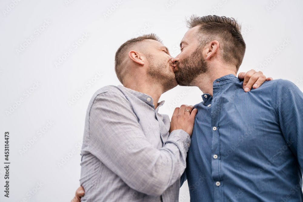 Cheerful couple of gays kissing under light sky Cheerful couple of gays kissing under light sky