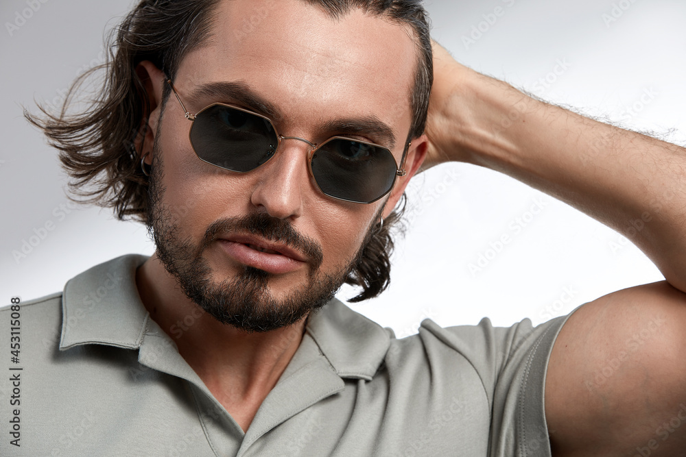 Brutal man in sunglasses, close-up, brunette with stubble in stylish glasses on a gray background Brutal man in sunglasses, close-up, brunette with stubble in stylish glasses on a gray background