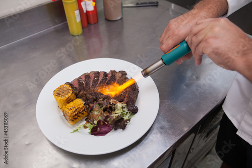 Unrecognizable chef flambing grilled ribeye steak with blowtorch photo