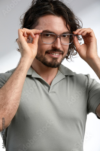 Handsome, smiling, young man with dark long hair and stylish glasses isolated on gray background, in stylish clothes, positive and success in career and business.