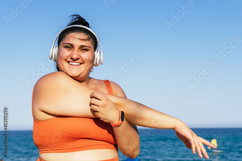 Smiling overweight ethnic sportswoman in headset under a blue sky