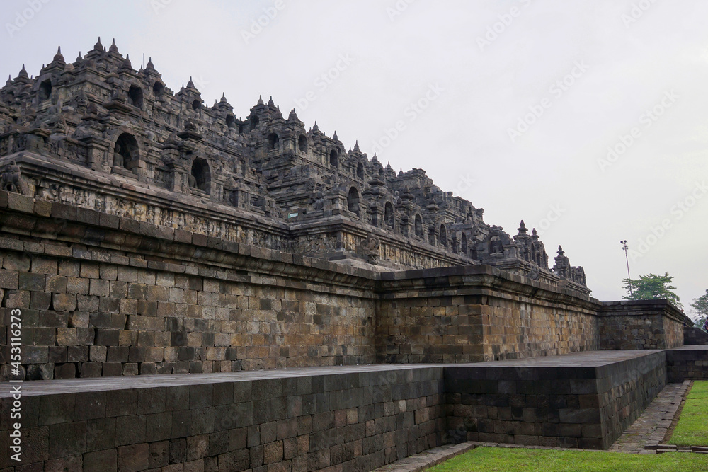 Exterior wall of ancient Borobudur temple view from the base of temple with clear blue sky. No people. Popular tourist and Buddhist pilgrimage destination.