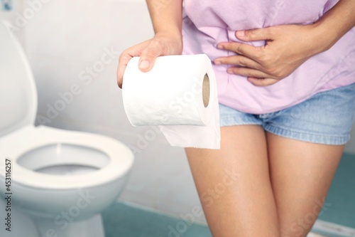 A woman wearing a pink shirt carries toilet paper to the toilet.