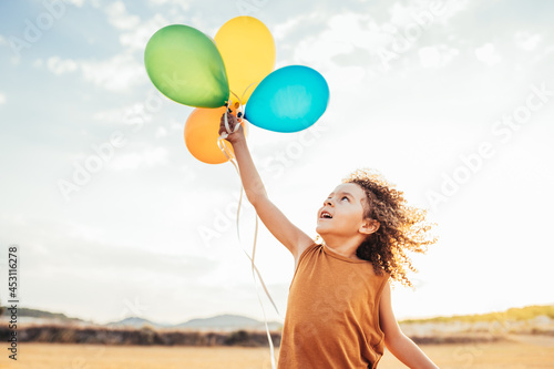 Carefree ethnic child playing with colorful balloons in field