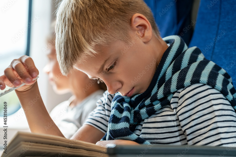 Happy children travels on train returns to home from holidays. Boy prepare to Back to school. Thoughtful Boy reads book. Happy girl sits by window in background Happy children travels on train returns to home from holidays. Boy prepare to Back to school. Thoughtful Boy reads book. Happy girl sits by window in background