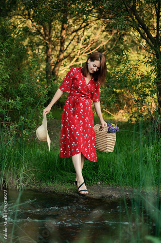 Fototapeta Naklejka Na Ścianę i Meble -  JOMO, joy of missing out, Connecting with nature, mental healing, mental health, calmness concept. Young woman in red dress and straw hat walks alone in the forest