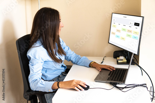 Latina Female Specialist Working on Desktop Computer at Home Living Room while Sitting at a Table. Freelancer Female Checking Her Calendar to Make an Appointment with New Clients and Employer.
