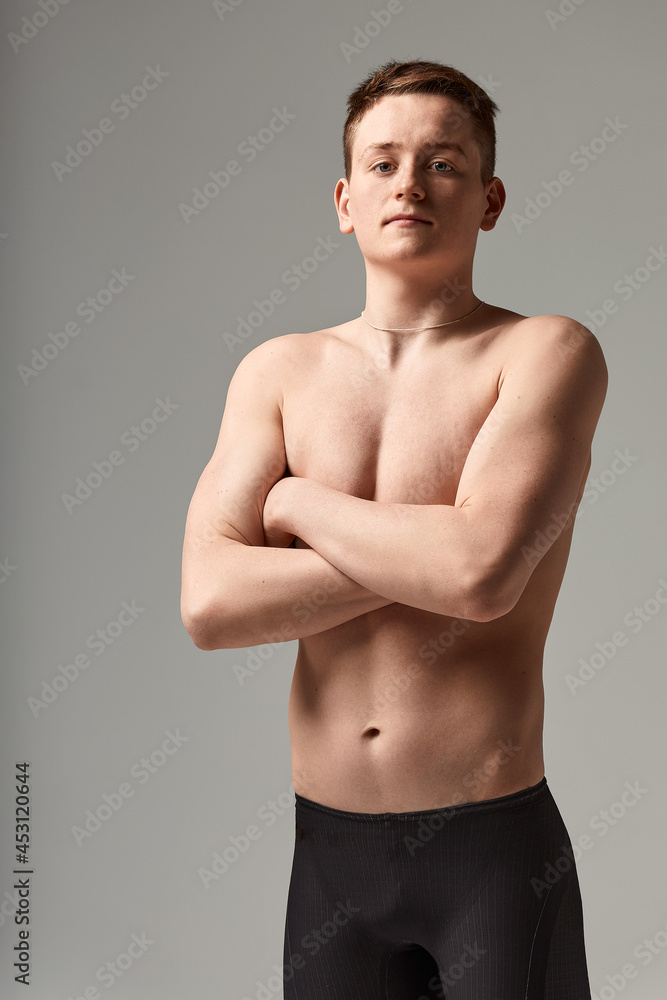 Young attractive swimmer in excellent physical shape in purple swimming shorts, on a gray background, copy space