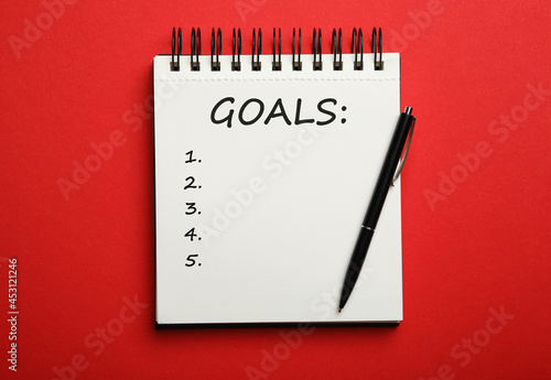 Pen and notebook with inscription GOALS on red background, top view. New Year aims © New Africa