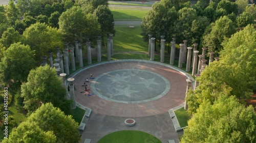Aerial tilt down reveals carillon pillars and people doing yoga. Tennessee state emblem, logo.
