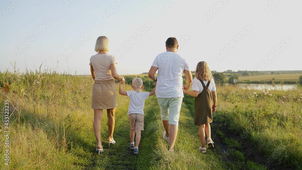 View of a beautiful cheerful family walking with children, spending daytime in a cottage town on weekends outdoors. In the summer, a happy family walks in the cottage village. View of a beautiful cheerful family walking with children, spending daytime in a cottage town on weekends outdoors. In the summer, a happy family walks in the cottage village.