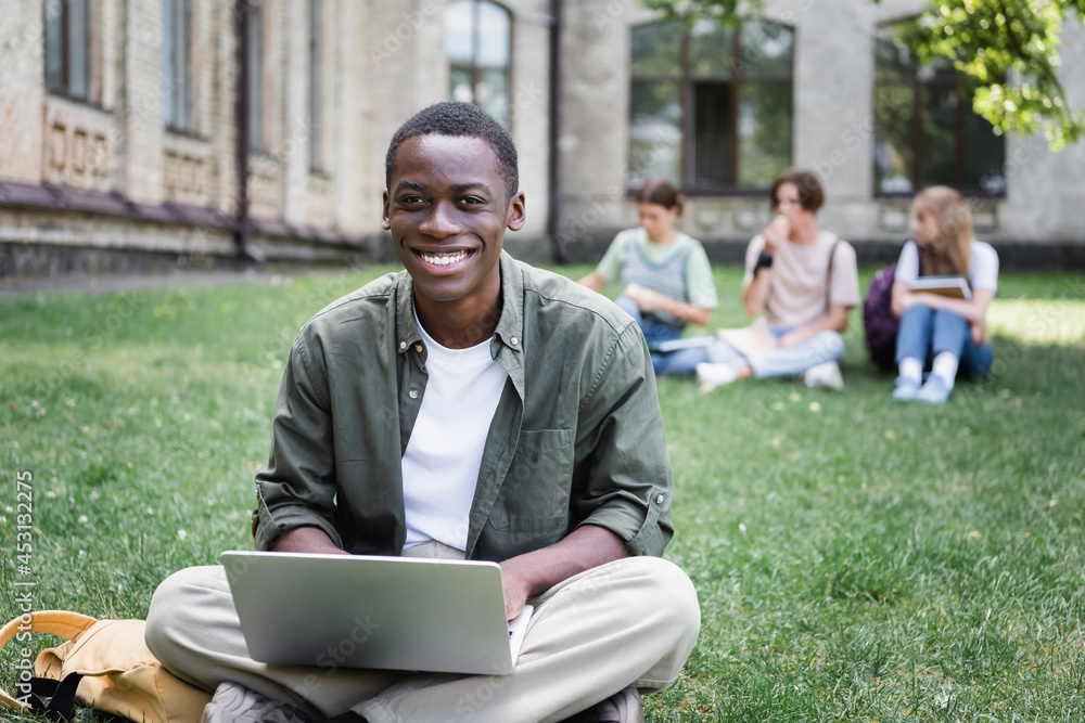 Cheerful african american student using laptop on lawn outdoors Cheerful african american student using laptop on lawn outdoors