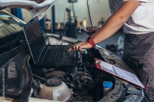 Professional car mechanic working in auto repair service using laptop.