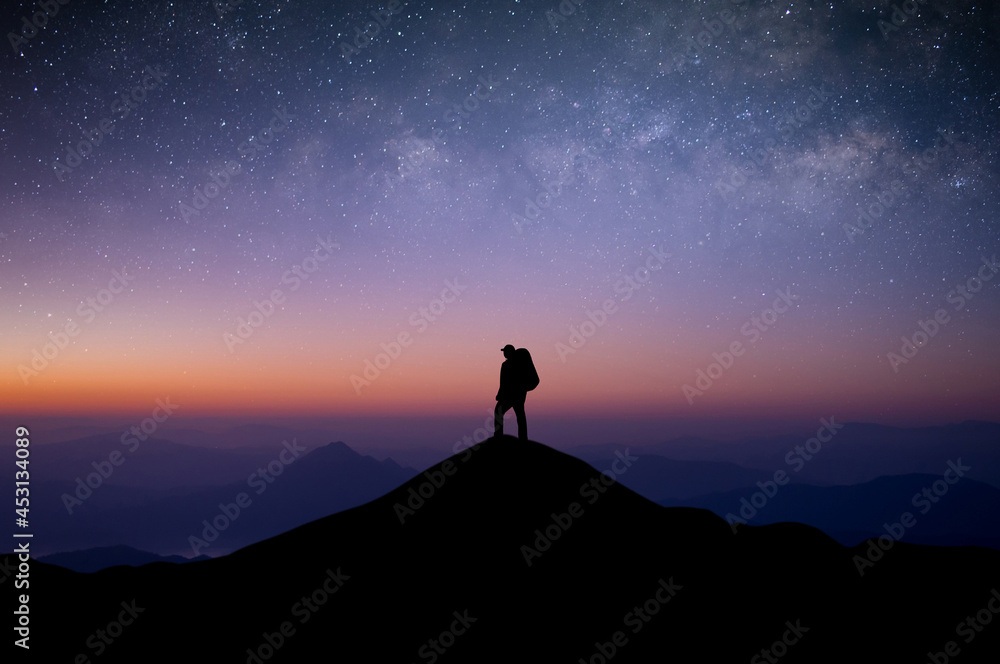 Silhouette of young man traveler with backpack standing and watched the star and milky way alone on top of the mountain. He enjoyed traveling and was successful when he reached the summit.