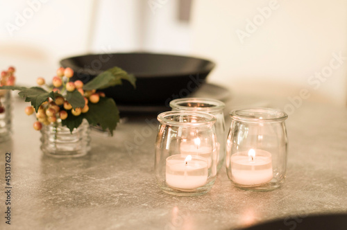 Candles in the small glass jars on the table with berries and plate in the background.