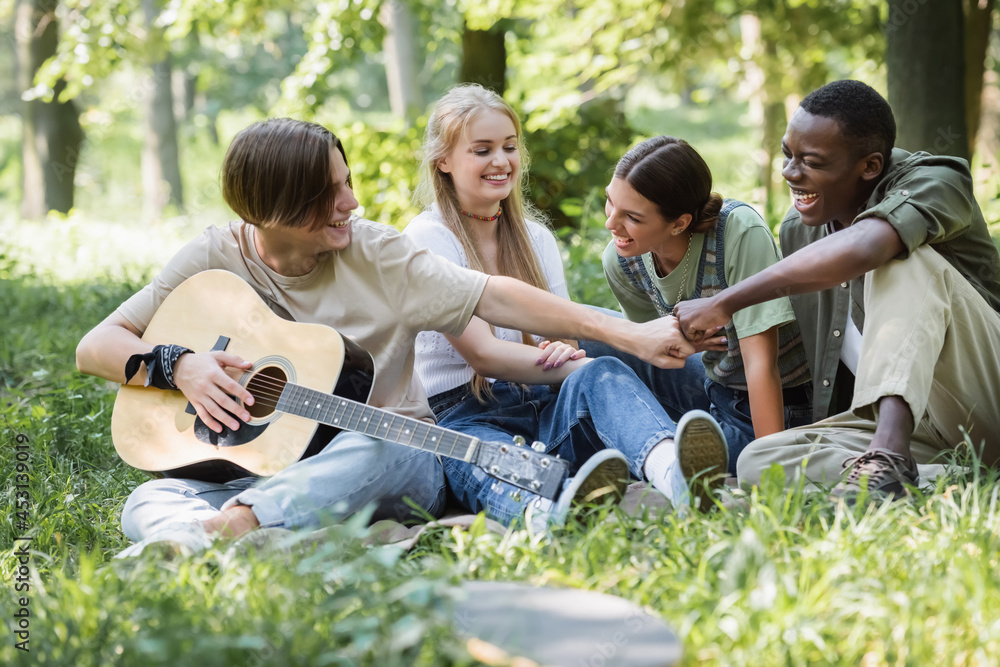 Interracial teenagers with acoustic guitar doing fists bump in park Interracial teenagers with acoustic guitar doing fists bump in park