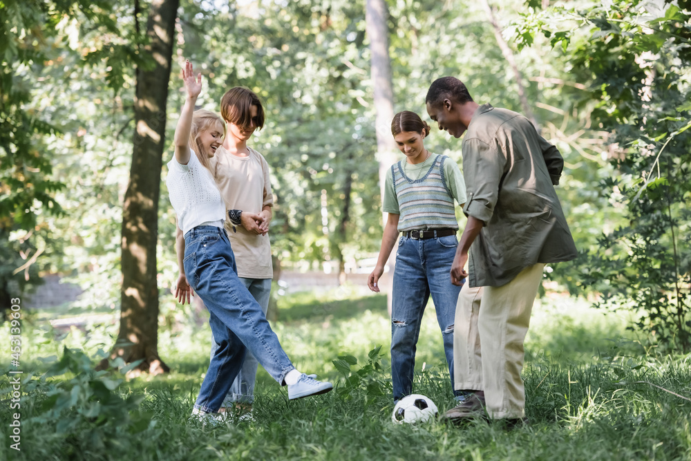 Obraz premium Cheerful multiethnic teenagers playing football in park