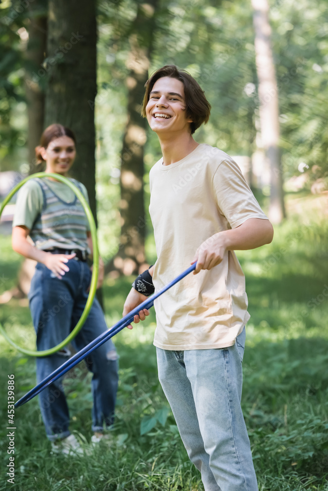 Positive teenager holding hula hoop near blurred friend