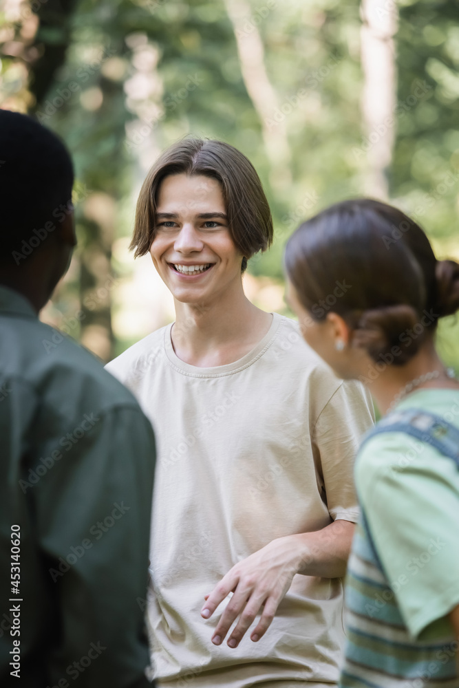Smiling teenager looking at blurred african american friend in park Smiling teenager looking at blurred african american friend in park