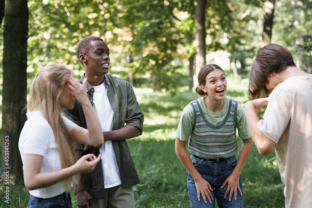 Smiling girl looking at friend near multiethnic teenagers in park
