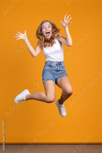 Surpise. Happy and cheerfull young woman jumping and laughing on orange background photo