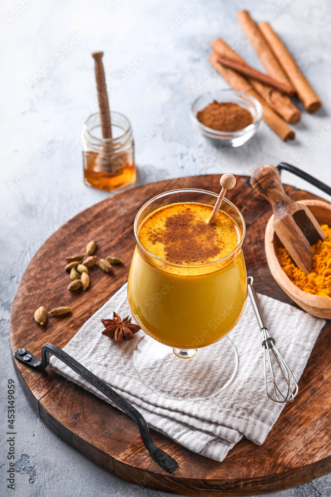 Turmeric golden milk latte with cinnamon sticks and honey. Healthy ayurvedic drink. Trendy Asian natural detox beverage with spices for vegans. Copy space. Turmeric golden milk latte with cinnamon sticks and honey. Healthy ayurvedic drink. Trendy Asian natural detox beverage with spices for vegans. Copy space.