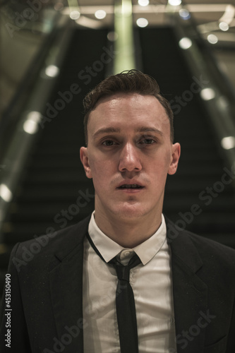 Close-up portrait of young handsome caucasian business man in elegant business suit with the tie stands near to escalator.