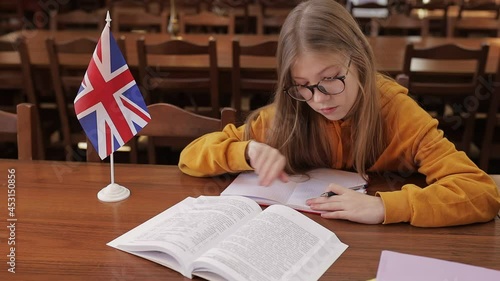 The student, the child writes, studies in the school library, the girl does her homework at the table, there is an American flag near the books. Study abroad concept. photo