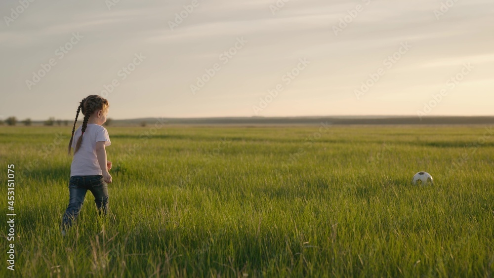 A small child kicks the ball on the field at sunset, a FIFA World Cup fan, a kid running on green grass dreaming of becoming a football player, preparing a baby for an adult final game