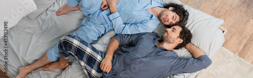 Foto top view of happy gay couple in pajamas resting on bed, banner