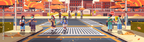 mix race schoolchildren in masks crossing road on crosswalk pupils walking to school coronavirus pandemic concept