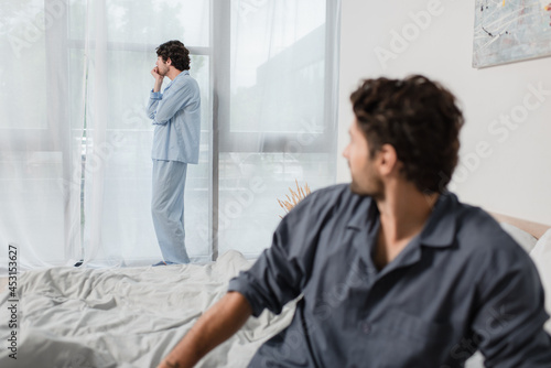 man standing and looking at window with blurred boyfriend on foreground, relationship difficulties concept