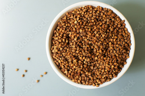 Dry buckwheat lies in a white bowl on a gray background. Healthy nutrition concept. Horizontal orientation. Buckwheat contains a large amount of vitamins and minerals. Top view. Copy space.