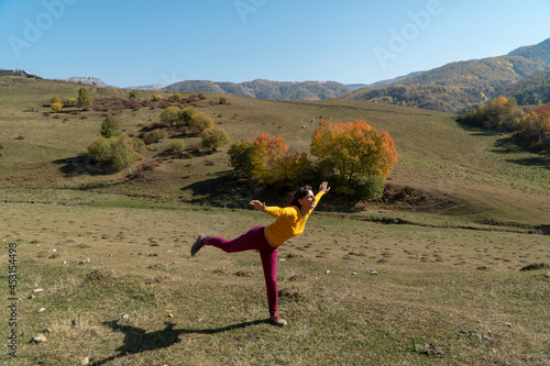 A woman in a good mood playfully makes a pose of a swallow in the mountains in autumn