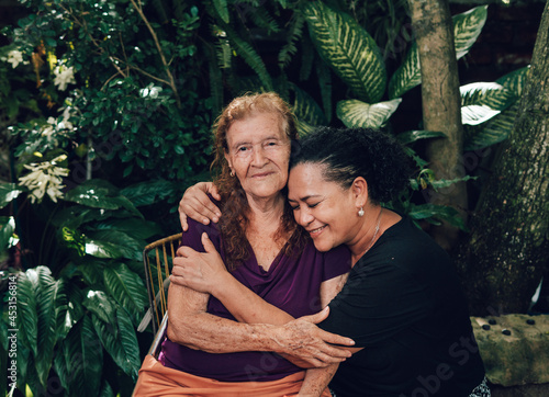 latin woman with curly hair hugging her old mother while smiling photo