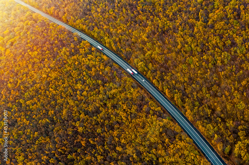 several trucks driving along a beautiful autumn highway across the autumn forest. cargo transportation. Cargo delivery. Sunset. Top view. Drone photo