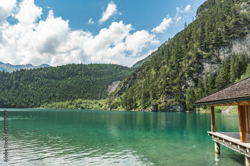 A boat shed and a view to an emerald green Blindsee lake surrounded by forest and mountains