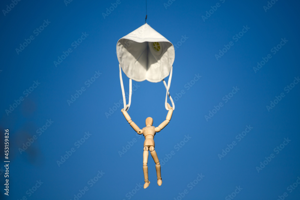 Fototapeta Wooden figure flying with respirator mask as parachute, destined to prevent the spread of the coronavirus, COVID-19.