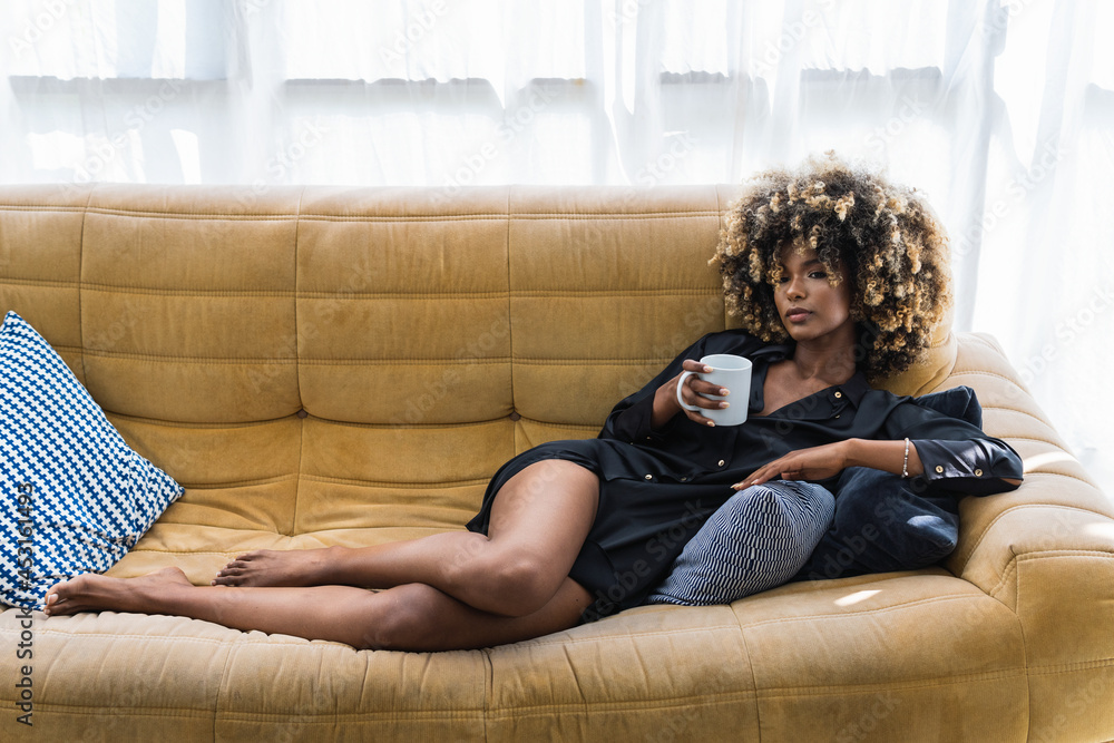 Black woman relaxing on couch with cup of drink Stock Photo | Adobe Stock